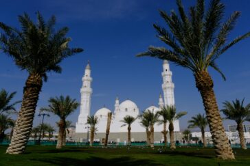 The historic Quba Mosque and palm trees under a clear blue sky in Madinah, Saudi Arabia.